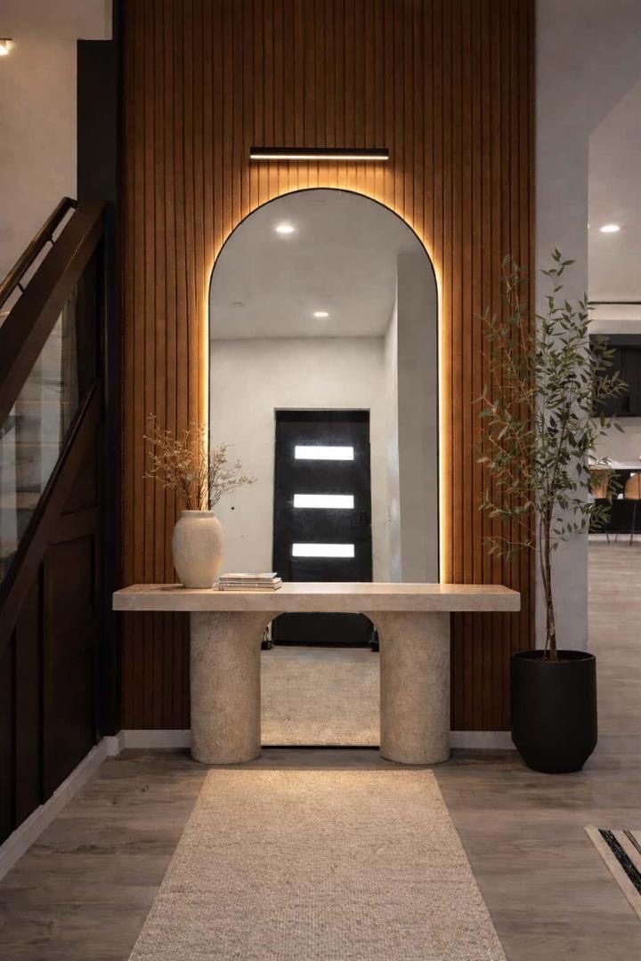 Warm entryway with wood-slat wall, arched mirror, console and olive tree by Lux Lustre Homes